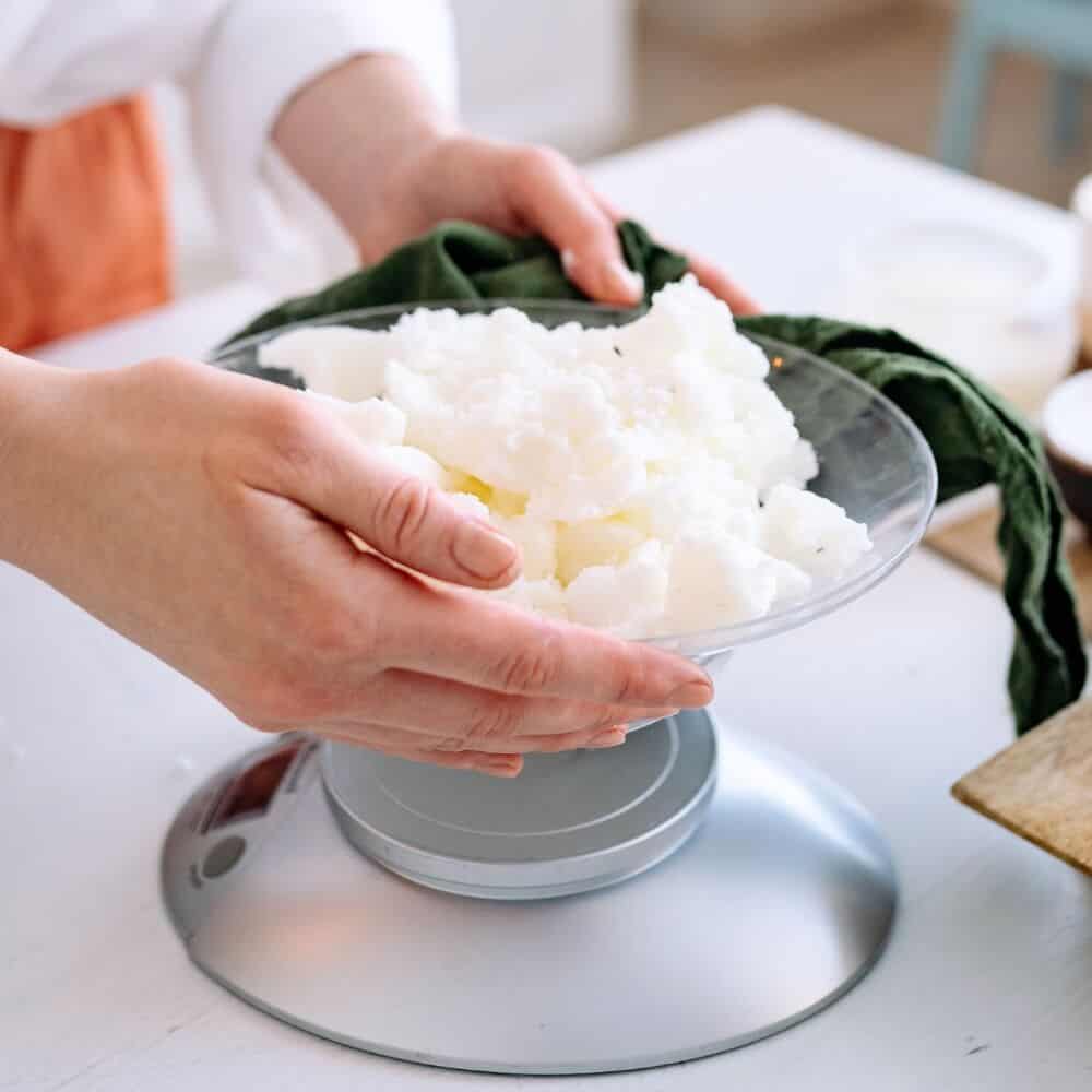 Hands measuring shea butter on a kitchen scale for a homemade skincare recipe